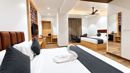 Bed with a black runner and towel art at Daksh The Royal Braj, Vrindavan, with a wall-mounted television and ceiling fan in the background.