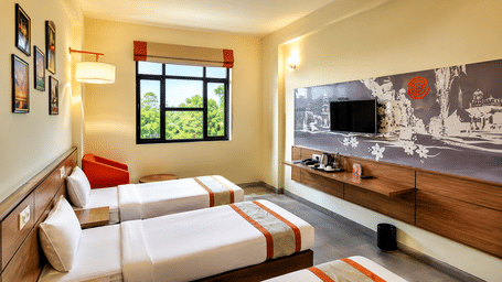 Max Club Room at Max Hotel Jabalpur with twin beds, a seating area, wall mounted TV and large window.