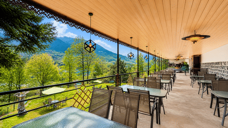 Opal bar at Orsino Khangri Karpo Retreat & Spa, Lachung featuring a row of dining tables with chairs faces a mountain view. The space has a wood-panelled ceiling and hanging lights.