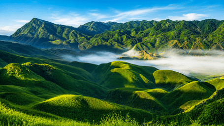 Lush green mountain valley with morning mist floating between rolling hills under a bright sky.