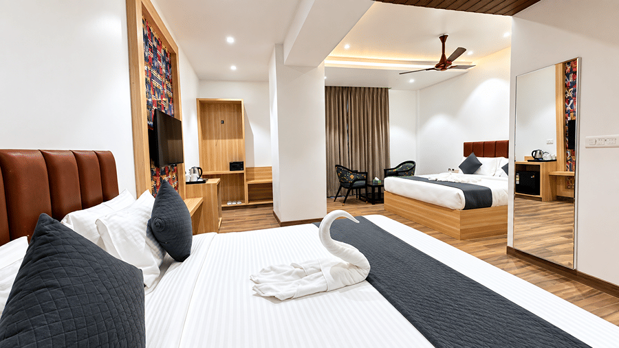 Bed with a black runner and towel art at Daksh The Royal Braj, Vrindavan, with a wall-mounted television and ceiling fan in the background.