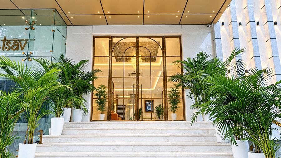 Entrance of Daksh The Royal Braj, Vrindavan, with steps leading to glass doors, flanked by potted plants.