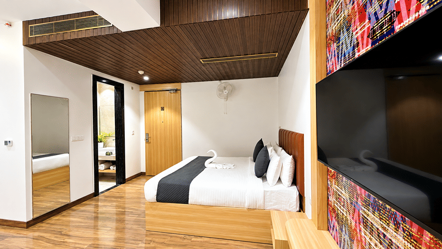Room at Daksh The Royal Braj, Vrindavan, with a bed, a wall-mounted television on a colourful panel, and wooden flooring.