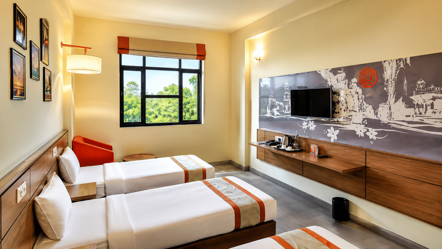 Max Club Room at Max Hotel Jabalpur with twin beds, a seating area, wall mounted TV and large window.