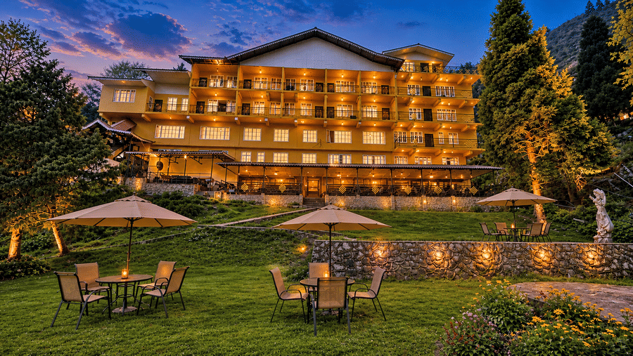 The exterior of Orsino Khangri Karpo Retreat & Spa, Lachung at dusk with lights glowing from the windows and an outdoor seating area on a lawn with tables and umbrellas.