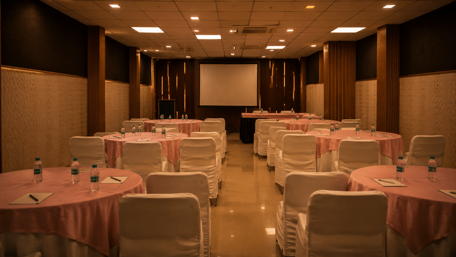 A banquet hall with chairs and tables arranged for an event with a display screen on the wall. | The Pamposh, New Delhi.