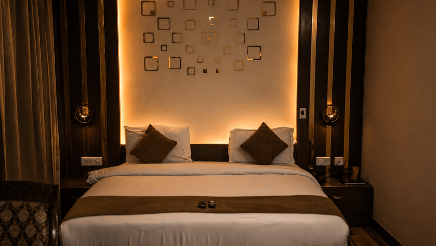 The Pamposh, New Delhi | A room with tables, a chair, a large bed, sporeads, pillows, and decorated wall.