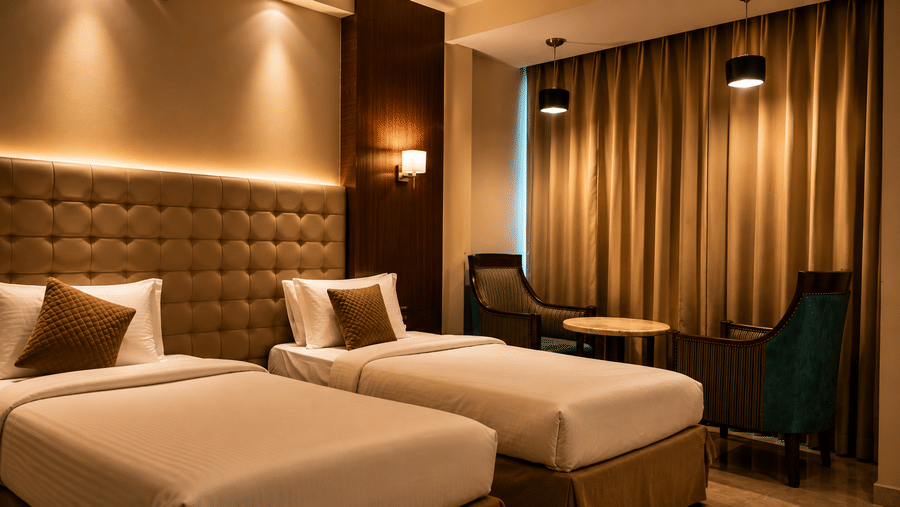 The Pamposh, New Delhi | A room with tables, a chair, a twin beds, sporeads, pillows, and decorated wall.