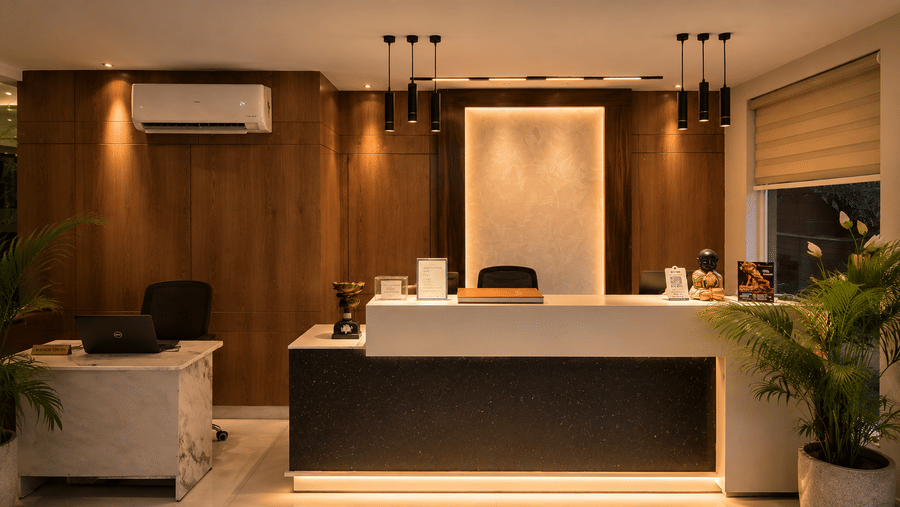A reception area at The Pamposh, New Delhi, with desks, air-conditioner, a chair, and a plant.