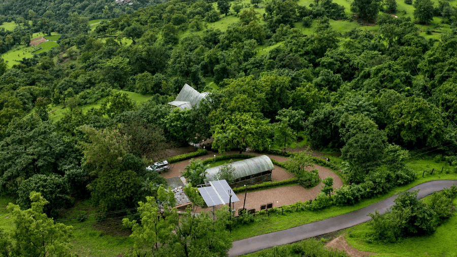 Aerial view of Wind Chalet surrounded by dense forest, with chalet buildings, landscaped grounds, and a winding access road visible through the trees.