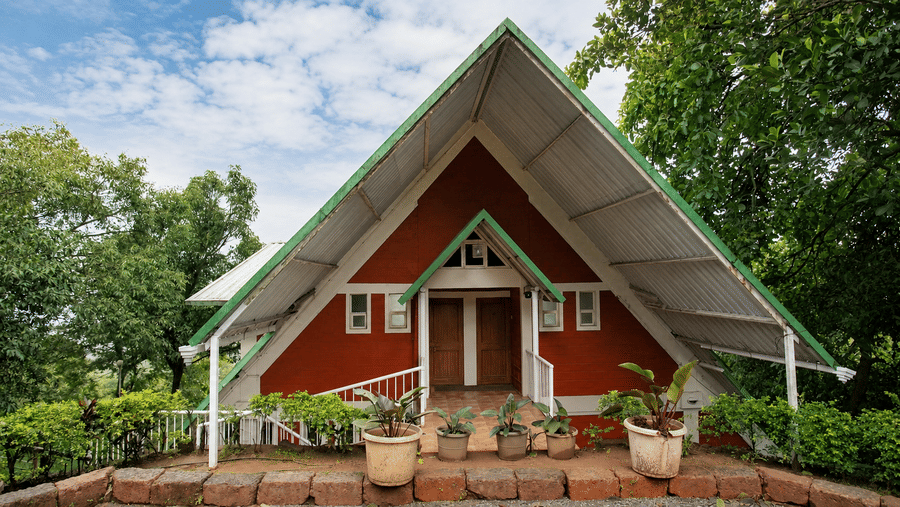Front view of an A frame chalet at Wind Chalet, featuring a steeply pitched roof, entrance porch, potted plants, and large windows.