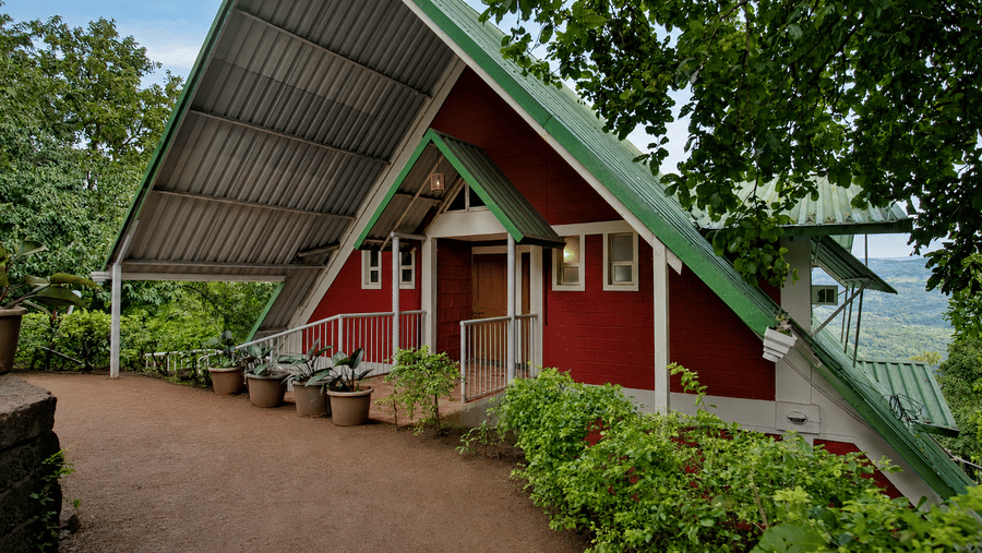 Side view of an A frame chalet at Wind Chalet, featuring a covered veranda, exterior walkway, entrance door, and landscaped garden.