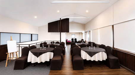 Banquet hall at Valmere Himalayan Hotel & Spa, Gangtok set up classroom-style with round tables, white tablecloths, dark chair covers, and a whiteboard easel.