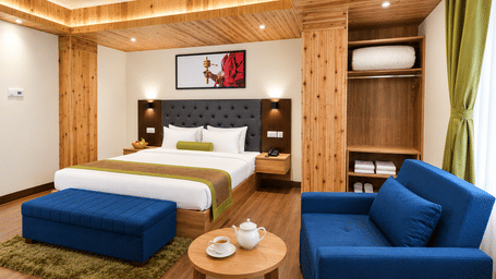 Guest room at Valmere Magnolia Boutique Hotel & Spa, Pelling with a bed, a navy sofa, a round tea table, and an open wardrobe with towels and a robe.
