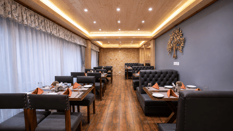 Restaurant hall at Valmere Magnolia Boutique Hotel & Spa, Pelling with black leather booths, tables set with orange napkins, and a metal tree on a blue wall.