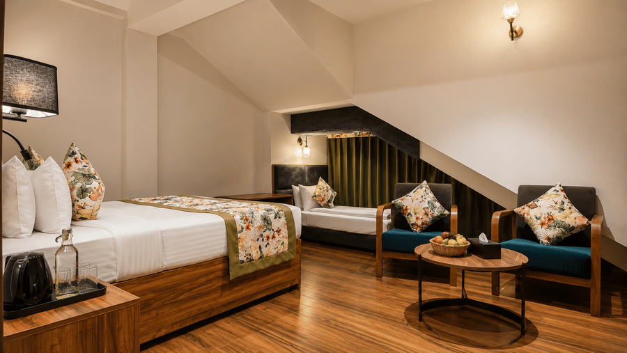 Room at Valmere Himalayan Hotel & Spa, Gangtok with 2 beds under a sloped attic ceiling, floral cushions, and a sitting area with 2 armchairs around a round table.