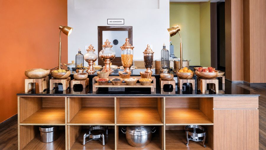 Buffet counter at Valmere Himalayan Hotel & Spa, Gangtok with copper jars of dry fruits and cereals, wooden bowls of nuts, and chafing dishes on warmers below.