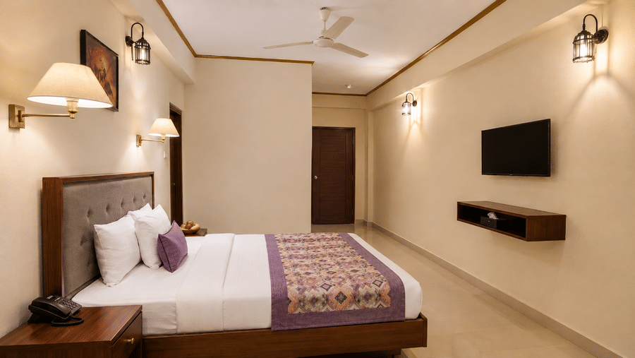 Family Room at Valmere Himalayan Hotel & Spa, Gangtok with a king-size bed, purple bolster pillow, wall-mounted TV, and a hallway leading to the bathroom door.