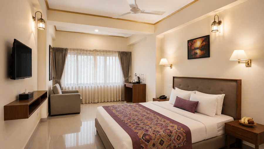 Family Room at Valmere Himalayan Hotel & Spa, Gangtok with a king-size bed, framed artwork, a grey sofa by the window, and a dresser with tea/coffee amenities.