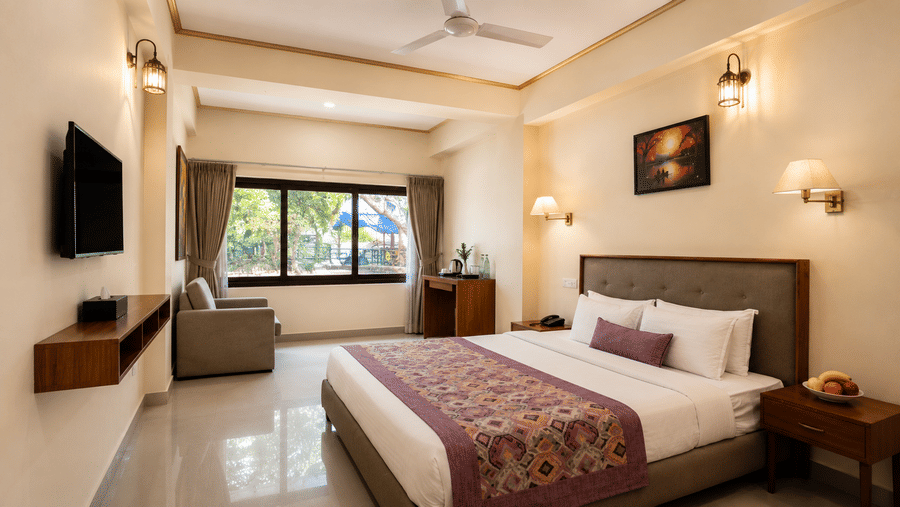 Family Room at Valmere Himalayan Hotel & Spa, Gangtok with a king-size bed, framed artwork above the headboard, a gray armchair, and a window overlooking greenery.