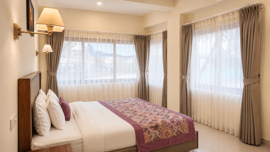 Family Room at Valmere Himalayan Hotel & Spa, Gangtok with a bed featuring a purple patterned runner, and large windows dressed with sheer and beige curtains.