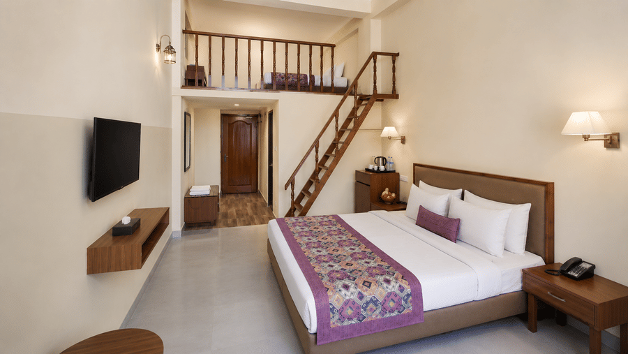 Family Suite at Valmere Himalayan Hotel & Spa, Gangtok with a king-size bed, wall-mounted TV, a wooden staircase, and a loft bed visible above the hallway.