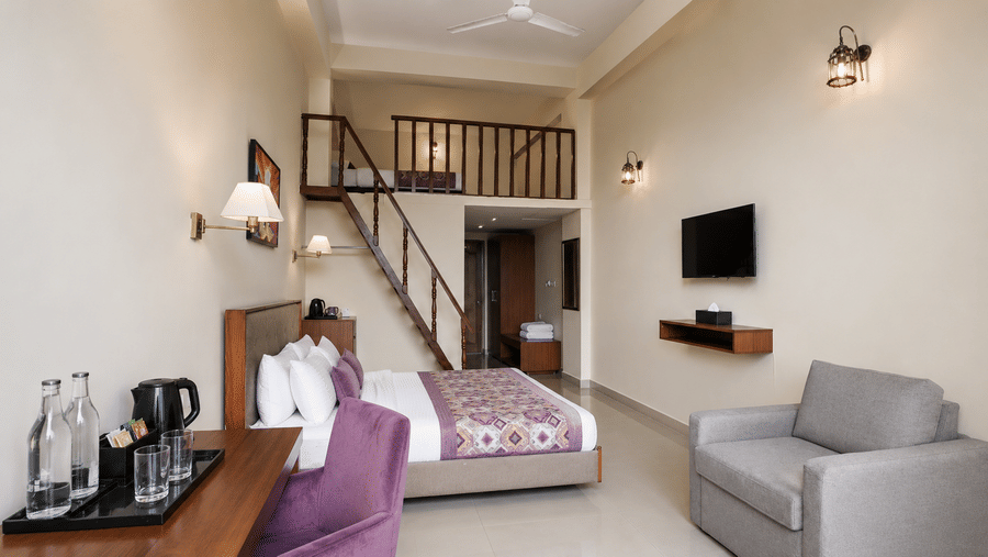 Family Suite at Valmere Himalayan Hotel & Spa, Gangtok with a king-size bed, a purple sofa, gray armchair, wall-mounted TV, and a staircase to the mezzanine loft.