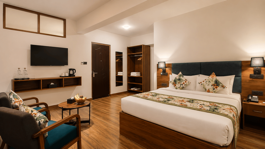 Guest room at Valmere Himalayan Hotel & Spa, Gangtok with a teal headboard, floral-patterned cushions, an open wooden wardrobe, and a sitting area with 2 armchairs.