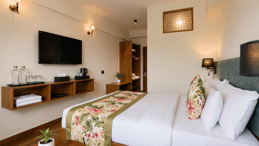 Guest room at Valmere Himalayan Hotel & Spa, Gangtok with a teal headboard, a floral-patterned bed runner, an open wooden wardrobe, and folded towels on a shelf.