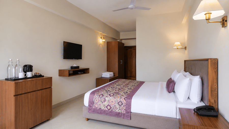 Guest room at Valmere Himalayan Hotel & Spa, Gangtok with a king-size bed, purple bolster pillow, an open wooden wardrobe, folded towels, and a wall-mounted TV.
