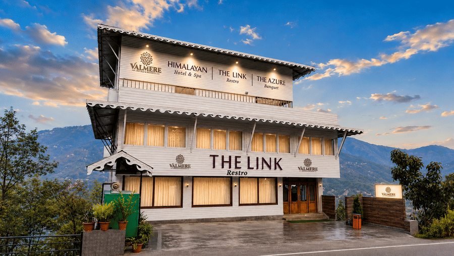 Exterior facade of Valmere Himalayan Hotel & Spa, Gangtok at dusk, showing The Link restro and The Azure banquet signage against a mountain backdrop.
