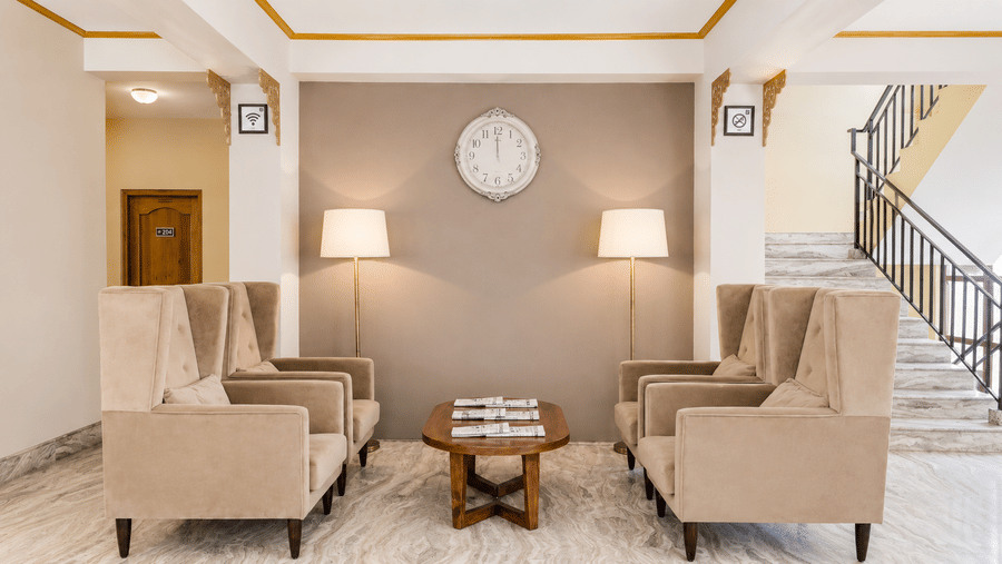 Lobby seating area at Valmere Himalayan Hotel & Spa, Gangtok with 4 beige wingback armchairs, a round wall clock, 2 floor lamps, and a wooden coffee table.