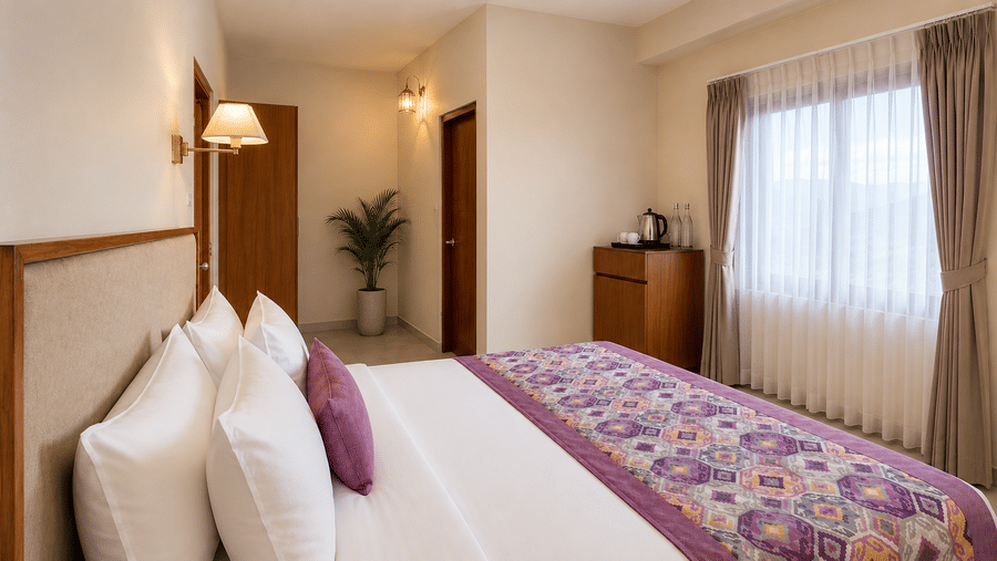 Suite bedroom at Valmere Himalayan Hotel & Spa, Gangtok with a king-size bed, 4 pillows, a wooden wardrobe, a potted plant, and a large window with mountain views.