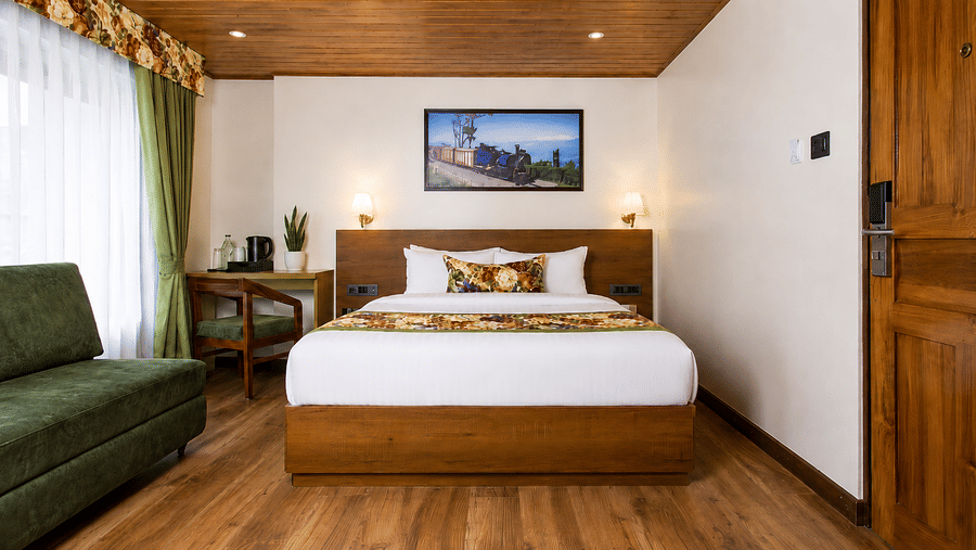 A king size bed, a sofa, a desk with a chair, and a framed picture on the wall in a hotel bedroom at Valmere Lungta Boutique Hotel & Spa, Darjeeling.