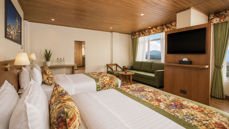 2 double beds, a sofa, a coffee table, a wall mounted television, and a window at Valmere Lungta Boutique Hotel & Spa, Darjeeling.