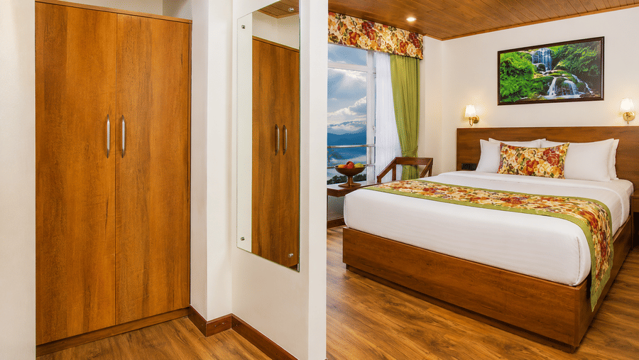A double bed, a tall wooden wardrobe, a full-length wall mirror, and a window view at Valmere Lungta Boutique Hotel & Spa, Darjeeling.