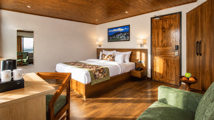 A king size bed, a sofa, a wardrobe, and a wooden furnished bedroom at Valmere Lungta Boutique Hotel & Spa, Darjeeling.