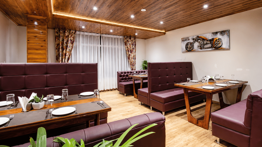 A dining space with plush leather booth seating, wooden tables, cutlery, and wall decor at Valmere Lungta Boutique Hotel & Spa, Darjeeling.