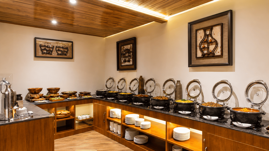 A buffet counter lined with 10 chafing dishes, stacked plates, bowls, and wall artwork at Valmere Lungta Boutique Hotel & Spa, Darjeeling.