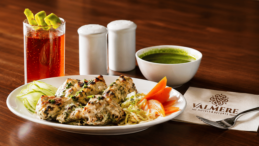 A plate of grilled chicken tikka served with sliced cucumbers, carrots, green chutney, and a beverage at Valmere Lungta Boutique Hotel & Spa, Darjeeling.