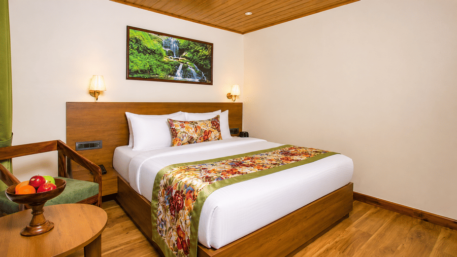 A double bed with floral textiles, a framed wall artwork, a wooden chair, and a fruit bowl at Valmere Lungta Boutique Hotel & Spa, Darjeeling.