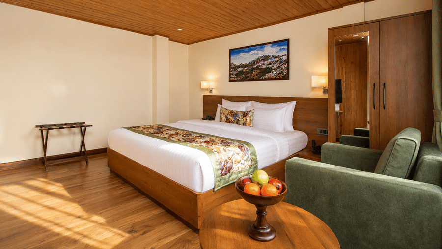 A king size bed, 2 armchairs, a wooden coffee table with a fruit bowl, and a wardrobe in a hotel room at Valmere Lungta Boutique Hotel & Spa, Darjeeling.