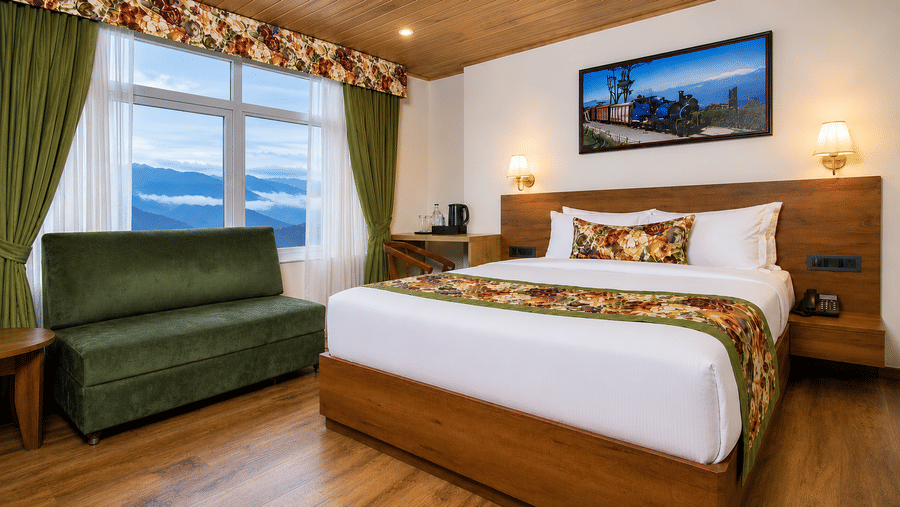 A king size bed, a sofa, a writing desk, and a window with mountain views in a hotel bedroom at Valmere Lungta Boutique Hotel & Spa, Darjeeling.