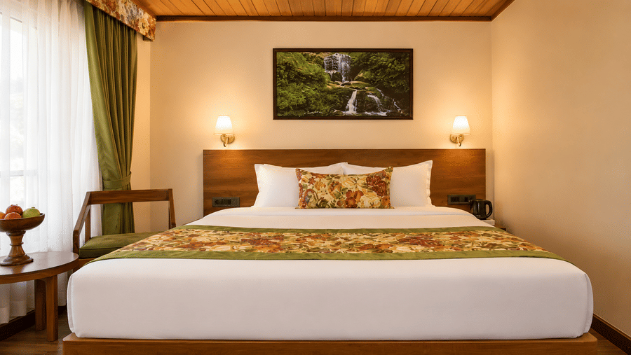 A king size bed, twin bedside lamps, a framed wall painting, and a small wooden coffee table at Valmere Lungta Boutique Hotel & Spa, Darjeeling.
