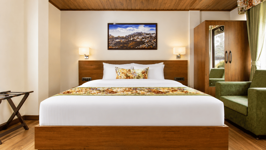 A king size bed, bedside lamps, a wardrobe, an armchair, and a wall picture at Valmere Lungta Boutique Hotel & Spa, Darjeeling.