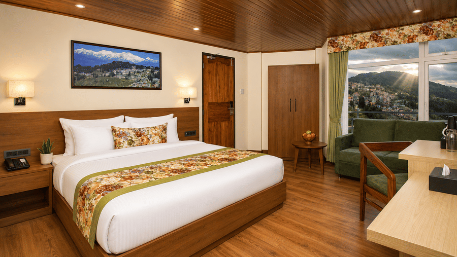 A king size bed, a sofa, a wardrobe, and a study desk with a wooden chair in a hotel bedroom at Valmere Lungta Boutique Hotel & Spa, Darjeeling.