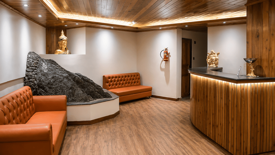 A curved wooden reception desk, tufted leather sofas, a rock feature, and a statue at Valmere Lungta Boutique Hotel & Spa, Darjeeling.