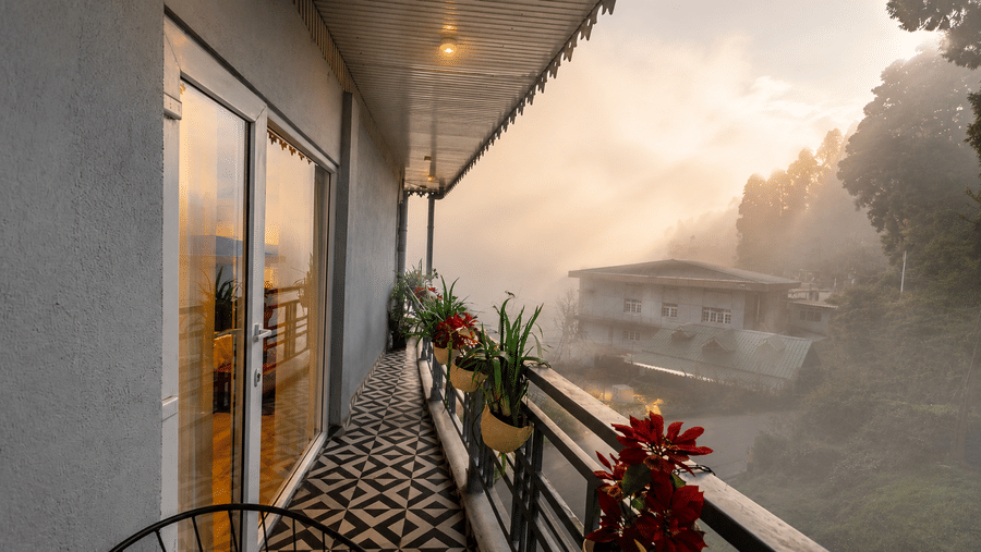Balcony corridor with potted plants, glass door, and mountain backdrop at Valmere Lungta Boutique Hotel & Spa, Darjeeling.