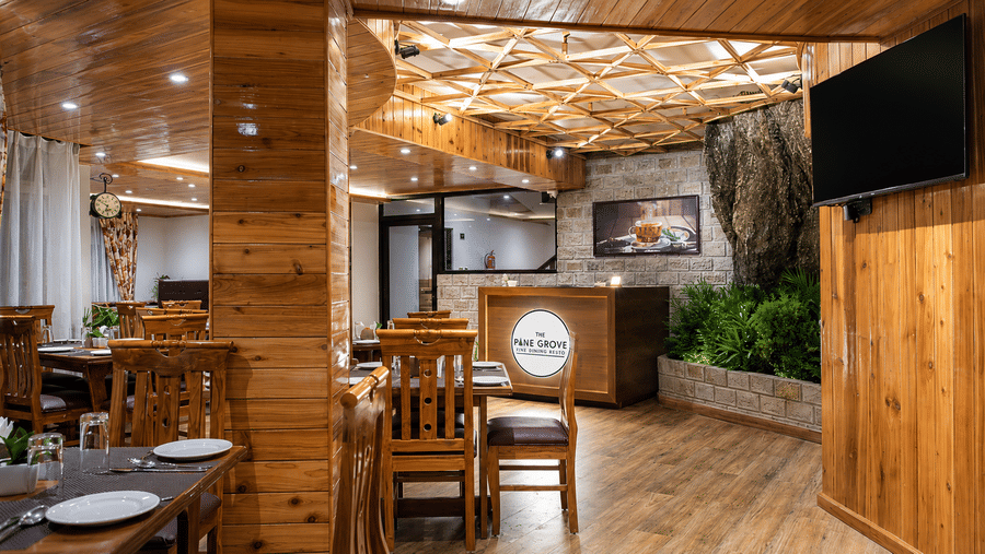 An indoor dining hall featuring wooden columns, tables, chairs, and a television on the wall at Valmere Lungta Boutique Hotel & Spa, Darjeeling.