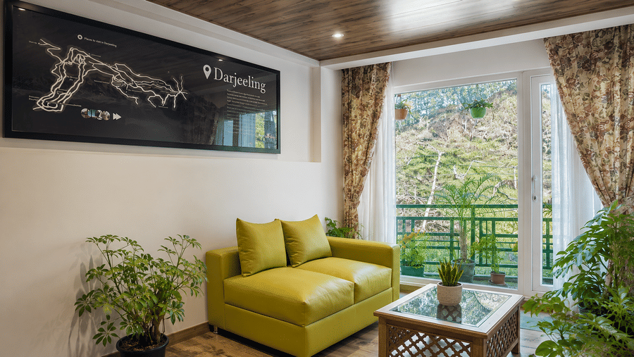 A sitting area with a 2-seater sofa, a coffee table, indoor plants, and a framed wall map at Valmere Lungta Boutique Hotel & Spa, Darjeeling.